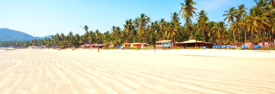 Solbeskinnet strand med palmer og farverige hytter langs kysten.
