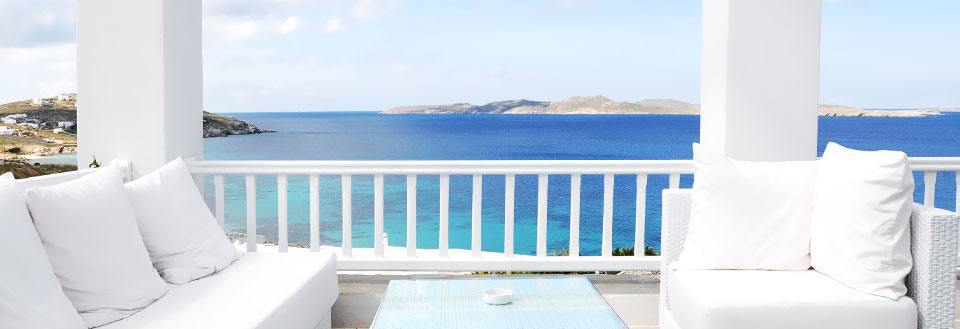 Billedet viser en terrasse med hvid sofa og puder med udsigt over en klar blå hav og himmel.