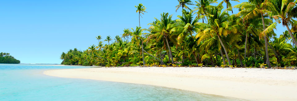 En idyllisk strand med fint hvidt sand, omgivet af vajende palmer og klart turkis hav.