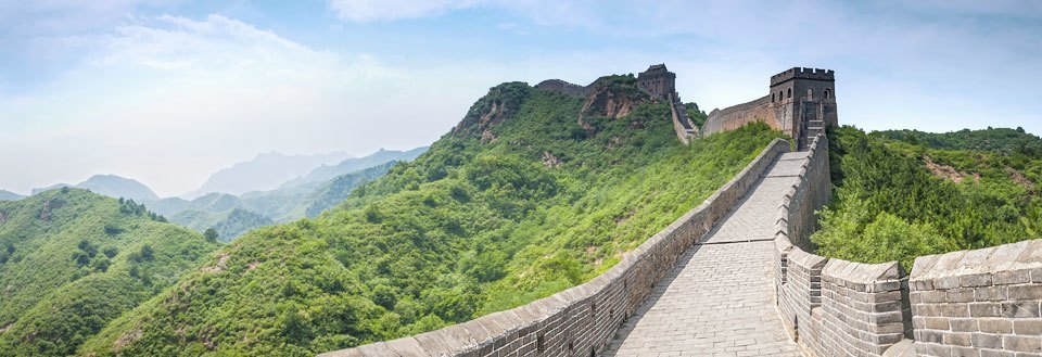 Billedet viser en storslået udsigt over Den Kinesiske Mur, der snor sig gennem et frodigt, grønt landskab.
