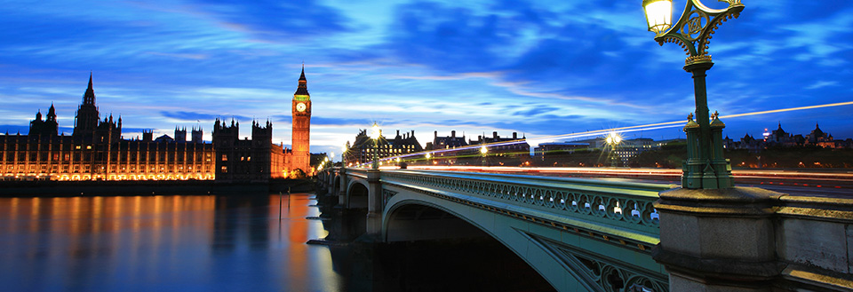 Aftenbillede af Westminster Bridge og Big Ben i London med lysstråler fra køretøjer.