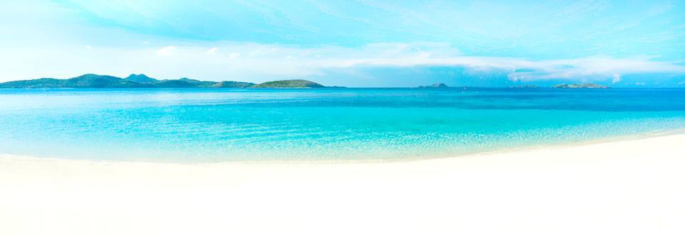 En malerisk strand med turkisblåt hav og himmel samt fjerne øer.
