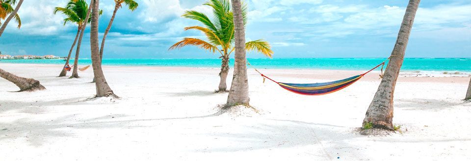 Farverig hængekøje mellem palmer på en hvid sandstrand og klar blå himmel.