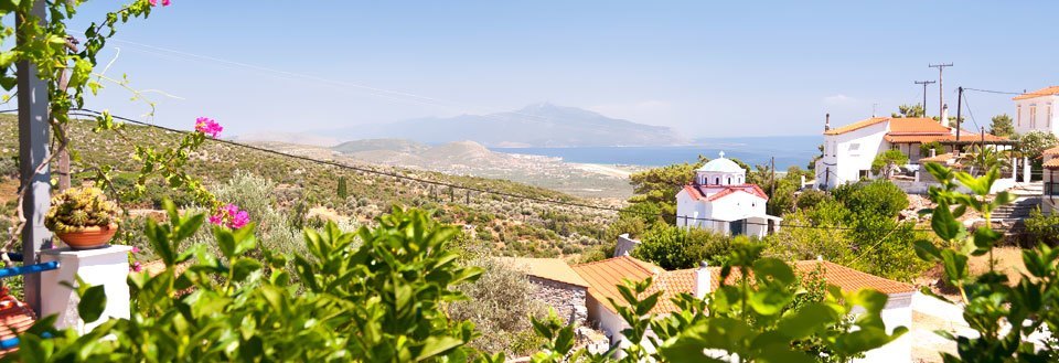 En idyllisk landsby med hvide huse på Samos, grønne områder og en kirke, med bjerge i baggrunden.