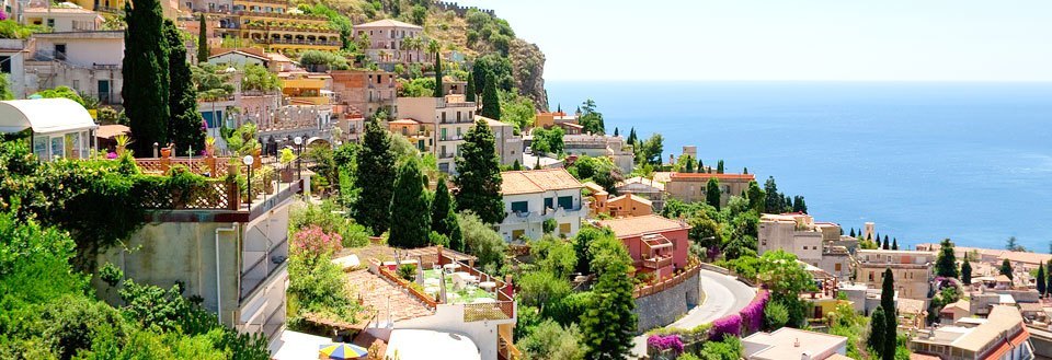 En malerisk kystby med tæt bebyggelse, frodige terrasser og azurblåt hav.