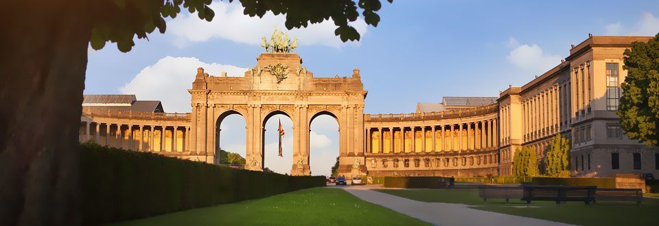 En stor triumfbue med skulpturer og kolonner badet i aftensol, flankeret af klassiske bygninger.