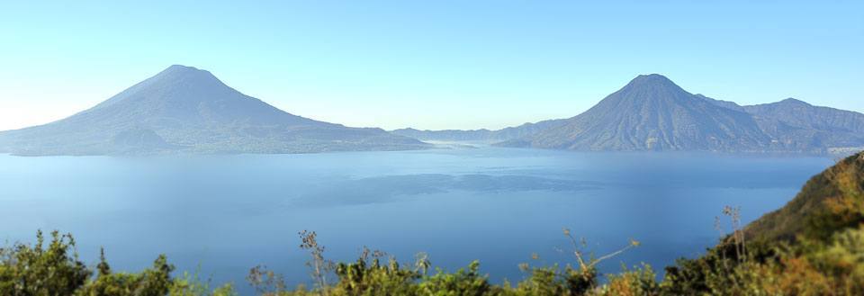 Panorama af en fredelig sø med omgivende bjerge og klar blå himmel.